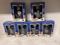 Five Hallmark Keepsake Snowman's Land ornaments in original boxed packaging with blue snowflake design and wooden fence motif.