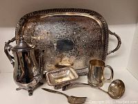 Photo of ornate serving tray with detailed engraving and rope handles alongside other serving pieces