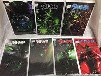 Photo showing all eight Spawn comic books arranged in two rows, each in clear protective sleeves, featuring cover art in dark and vivid colors.