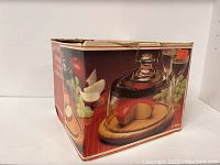 Image of the original box showing the product with cheese on a teakwood base and a glass dome cover.