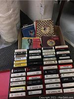 Photo showing several rows of 8 track tapes with one box holding 45 RPM vinyl records with visible record sleeves of George Benson and others.