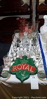 Table display of assorted branded shot glasses and crystal stemware arranged around a green breweriana sign with 'Royal' in red.