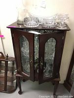 Front view of wood and glass display cabinet with two glass panel doors open, showing mirrored back and glass shelves inside.