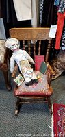Photo showing vintage child's wooden rocking chair with carved backrest and upholstered pillow seat. Chair holds a porcelain composite chef doll, multiple antique books including Edgar Allen Poe Little Library book, prayer book, and mini tops book with a top attached, along with mini wall plaques and small decorative items.