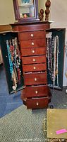 Full front view of wooden jewelry chest with drawers open and side cabinets displaying hanging necklaces