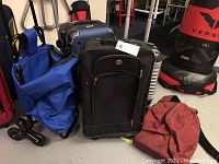 Group photo showing a black soft suitcase, blue collapsible cart, black backpack, red bag, and a silver hard shell case background.