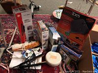 Photo of assorted boxed and unboxed home goods including warming footrest, handheld sewing machine, cleaning appliance, and fabric items.