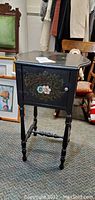 Photo showing black lacquer humidor with tole floral accents on door, turned legs, and visible scratches