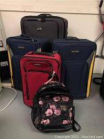 All five items grouped: Gray Rugged Cargo suitcase, two blue Nautica suitcases, one red Travelers Club suitcase, and one black Mossino floral backpack.