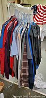 Photo showing variety of men's clothing on hangers including jackets, shirts, hoodies, casual and dress shirts in various colors and styles