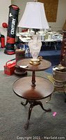 Full view of two-tiered mahogany pie crust table with claw feet, porcelain lamp on top