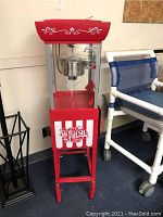 Full view of red Nostalgia Hot & Fresh electric popcorn machine on a stand with wheels, featuring glass panels and decorative text.