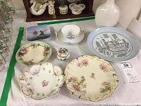 Top-down view of all items laid out on a white cloth showing wall hanging plates, cup and saucer, candy dishes and trinket box