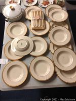 Overview of 15 ivory Syracuse China bowls and plates with gold decorative rims, lidded serving dish, and cutlery set in fitted case on table.
