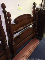 View of the wooden twin bed frame parts stacked against a wall, showing headboard, footboard, and side rails with carved details.