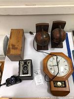 Photo showing the full lot on a table including globe bookends, wooden microscope box, vintage Brownie Target Six-20 box camera and Pentax camera, United Electric clock.