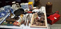 Wide view showing cast iron skillet, assorted vintage flatware, tins, figurines, and red toolbox tin.