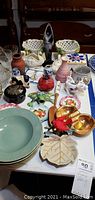 Overview of ceramic and pottery items including plates, bowls, figurines, and novelties arranged on table