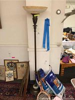 Full view of the vintage torchiere floor lamp standing against a wall with some nearby items, showing the bronze finish base, alabaster and brass weighted bottom, and peach and white globe.