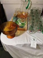 Collection of vintage glassware including amber candy dish, green dessert cups, clear pitcher with green handle, and Christmas tree glasses on round table.