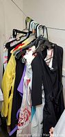 View of multiple women's clothing pieces hung on hangers including dresses, blouses, jackets showing various styles and colors