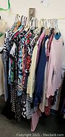 Clothes on hangers showing variety of patterned and solid blouses, tank tops, and dresses for women mostly small to medium sizes.