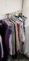 Photo of assorted women's clothing hanging on rack, showing variety of tops and outerwear.