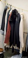 Six women's winter outerwear pieces hanging on rack including coats, sweaters, and jackets in various colors and textures.