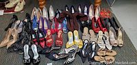 Photo showing various pairs of women's shoes arranged on floor in rows. Different styles, colors, and sizes visible.