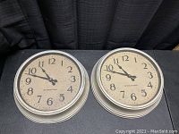 Front view of two 1930s International Ion school wall clocks with beige dial, black numerals and hands, silver metal frames.