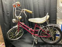 Full left side view of red Columbia muscle bike showing frame, banana seat, handlebars, speedometer, shifter, fenders and tires