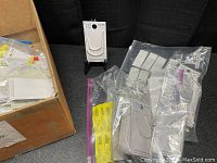 Box of assorted costume jewelry in plastic bags and retail packaging, showing various pieces mostly necklaces and earrings.