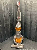 Full view of Dyson DC25 upright vacuum cleaner showing overall condition, handle, dust container, and attachments at the base.