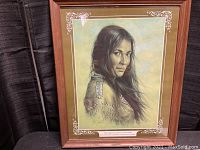 Framed Native American art print showing a portrait of a Native American woman with long dark hair and beaded shoulder decoration in wooden frame with green matting.