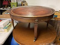 Full view of the round table showing the four tapered legs with brass casters and wooden apron with decorative rosettes.