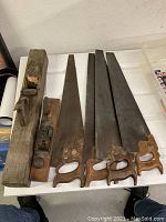 Photo showing four vintage wooden hand saws and two wood planes arranged on surface.