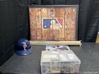 Wide shot showing the MLB logo poster, blue baseball helmet with 'P', rolled-up wooden bat, plastic card bin, and player posters.