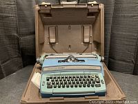Front view of the open vintage Smith Corona Super 12 Coronet typewriter in its brown plastic carrying case showing the keyboard and platen roller.