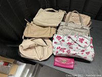 Six beige and white handbags and one pink wallet on a black surface, showing various styles and sizes.