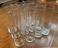 Set of twelve clear tall Stange beer glasses arranged in a group on a wooden surface, showing overall size, shape, and height.