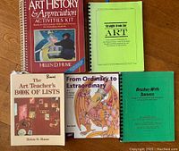 Five art education books arranged flat on a wooden surface with visible titles and covers showing.