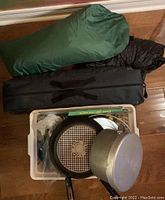 Photo shows packed green Eureka Timberline 2 person tent, black tarp and plastic bin with cooking pans and utensils.