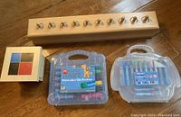 Photo of Montessori wooden toys including sorting game, math puzzle with pegs, and two sets of crayons in plastic cases on the floor.