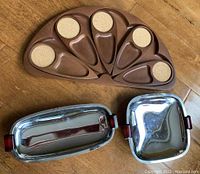 Teak peacock tray with six detachable trays next to two chrome and bakelite serving dishes on wood floor