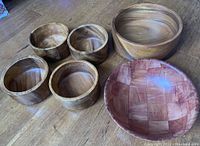 Six wooden salad and serving bowls grouped on wooden floor, showing size and finish variety