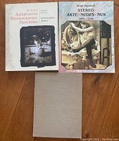 Three photography books arranged on wooden floor: 'The Book of Alternative Photographic Processes,' 'Stereo Akte • Nudes • Nus 1850-1930,' and a plain cloth hardcover book.