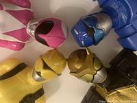 Close-up of four Power Rangers helmets (Pink, Blue, Yellow, Gold) showing detail and condition.