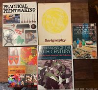 Top-down photo showing all 6 books arranged on a wooden surface. Covers visible include Practical Printmaking, Serigraphy, Batik Tie Dye Stenciling Silk Screen Block Printing, The Printmakers' Bible, Impressions of the 20th Century, and one more with colorful abstract art.