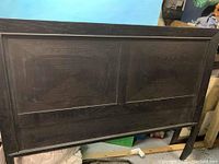 Front view of the solid wood queen headboard showing two large diamond-paneled sections with dark finish, minor wear and damage visible on surface.