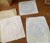 Photo showing three vintage 1980s iron-on transfers on tissue paper spread on a wooden surface, showing front and back views of the designs including ET, cartoon elephant, and unicorn.
